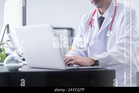 Junger asiatischer Arzt sitzt und arbeitet hart mit dem Computer Stockfoto