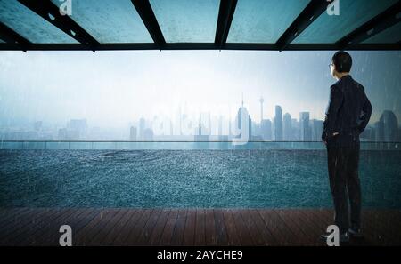 Geschäftsleute, die vor einem Swimmingpool auf dem Dach mit wunderschönem Blick auf die Skyline der Stadt blicken und denken Stockfoto