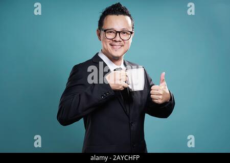 Geschäftsmann in Anzug lächeln und genießen Sie Kaffee mit Daumen oben-Geste. Stockfoto