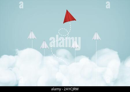 Ein einzigartiges rotes Flugzeug führt die Gruppe des weißen Papierflugzeugs am blauen Himmel und am Wolkenhintergrund an. Geschäfts- oder Designcrea Stockfoto