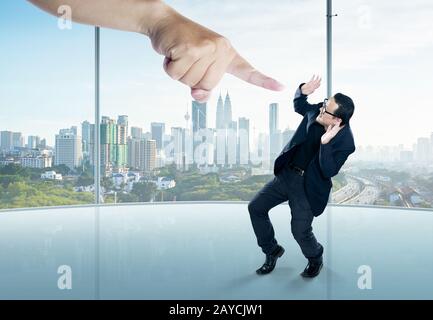 Ein erschrockter Geschäftsmann voller Höhe in einer Schreckstellung und einer riesigen Hand, die auf ihn zeigt Stockfoto