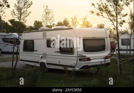 Wohnwagen und Wohnmobile auf grüner Wiese auf dem Zeltplatz. Sonnenaufgang, Strahlen auf den Campern am Morgen. Stockfoto