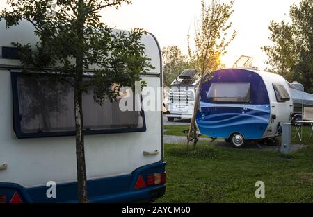 Wohnwagen und Wohnmobile auf grüner Wiese auf dem Zeltplatz. Sonnenaufgang, Strahlen auf den Campern am Morgen. Stockfoto