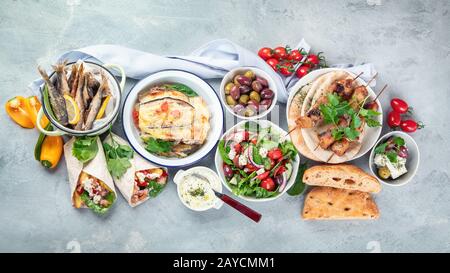 Griechische Speisen auf grauem Hintergrund. Moussaka, Gyros, Souvlaki, Pita, Salat, Oliven und Gemüse. Traditionelle griechische Gerichte. Draufsicht, fl Stockfoto