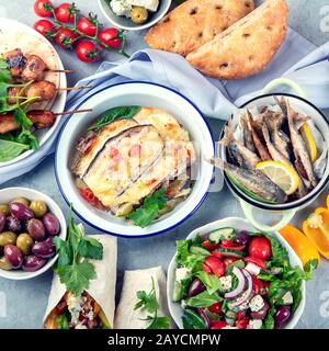 Griechische Speisen auf grauem Hintergrund. Moussaka, Gyros, Souvlaki, Pita, Salat, Oliven und Gemüse. Traditionelle griechische Gerichte. Draufsicht Stockfoto