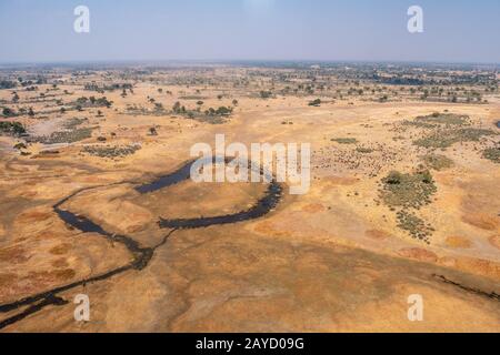 Okavango Delta Aerial mit trockener, gelber Ebene mit dunkelblauem Fluss in Moremi Game Reserve, Botswana, Afrika Stockfoto