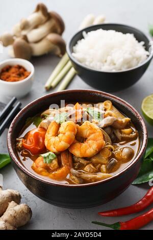 Traditionelle würzige thailändische Suppe Tom Yum Goong oder Tom Yum Kung und verschiedene Zutaten rund um. Serviert mit Reis. Stockfoto