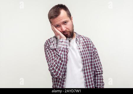 Portrait eines langweiligen jungen bärtigen Mannes im Plaid Hemd, das an der Hand mit dumpfem, faulen Gesichtsausdruck, depressiver, gleichgültig aussehender Optik, müde von allem. In Stockfoto