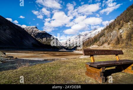 Bergtal mit Bach, Bäumen, Holzbank und getrocknetem Livigno-See, Alpen, Italien Stockfoto