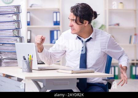 Junge männliche Mitarbeiter mit übermäßiger Arbeit unzufrieden Stockfoto