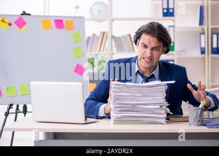 Junge männliche Mitarbeiter mit übermäßiger Arbeit unzufrieden Stockfoto