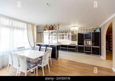 Weißer rechteckiger Tisch mit weißen Stühlen mit hohen Rückstützen im Küchenwohnzimmer des Laksheri-Cottages im klassischen Stil. Acht Stühle, große Fenster Stockfoto