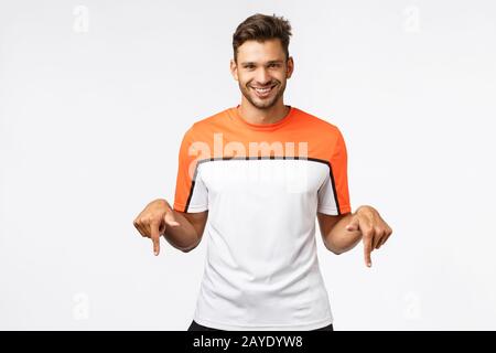 Gutaussehende freche, maskuline hispanische Sportlerin im Sport-T-Shirt, die Aktivewear trägt, laden Sie zum Kauf einer Fitness-Mitgliedschaft ein, lächelnd mystisch Stockfoto