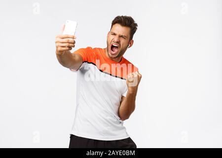 Zufriedene männliche Athletin im Sport-T-Shirt, die mit dem Preis ausgezeichnet wurde, die großartige Neuigkeiten, Errungenschaften von Social-Media-Anhängern und die Teilnahme mitteilt Stockfoto