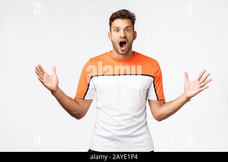 Aufgeregter, sprachloser, gutaussehender bärtiger junger Kerl in Sportbekleidung, mit Sport-T-Shirt, Fallbacke, Gasklatschen und Stare mit knalligem Ey Stockfoto