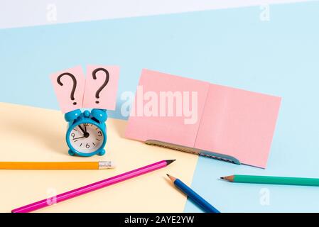 Kleiner Mini-Wecker neben dem stationären, gekippten Wecker. Notizpapier am Rand der leeren einfarbigen Tischkulisse. Stockfoto