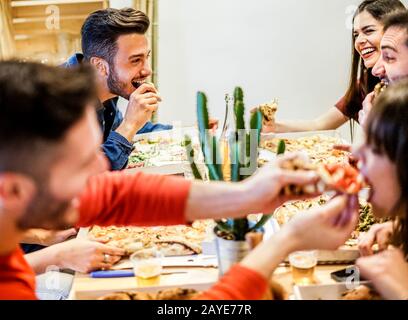 Eine Gruppe glücklicher Freunde, die zuhause Pizza essen - Junge Trendstudenten, die Spaß haben, beim Abendessen zusammen zu lachen - Konzentrieren Sich auf das Gesicht des linken oberen Mannes Stockfoto