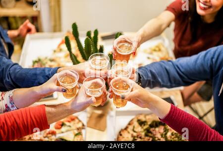 Eine Gruppe glücklicher Freunde jubelt zu Hause mit Bier - Junge Leute, die zusammen Spaß haben, italienische Pizza zu essen, nehmen weg - Abendessen, Party und Freundschaftskonz Stockfoto