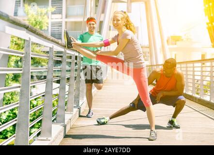 Eine Gruppe von Freunden, die sich ausstrecken, bevor sie in einer Brücke im Freien joggen - Multi Ethnic Fit People Training im städtischen Wettbewerb - neuer gesunder Lifestyle-Trend Stockfoto