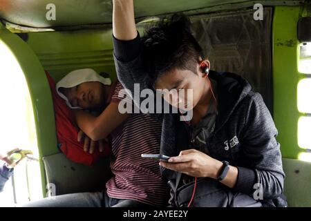 Antipolo City, Philippinen - 13. Februar 2020: Pendler schlafen und nutzen Smartphone innerhalb eines Passagierjeeps. Stockfoto