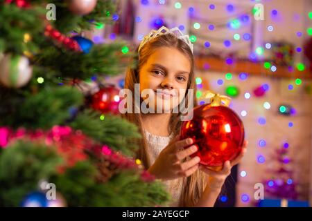 Schönsten zehn Jahre altes Mädchen peeking heraus mit einem großen roten Ball hinter einem Weihnachtsbaum Stockfoto