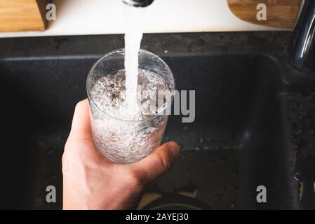 Füllung Glas Wasser aus Edelstahl Küchenarmatur. Trinkwasser Konzept Stockfoto