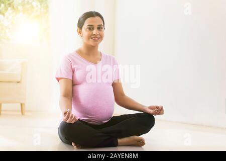 Schwangere Frau lächelt, während sie zu Hause Yoga praktiziert. Stockfoto