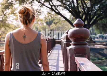 Junge blonde Frau von hinten auf einer Brücke in der Natur mit Tattoo auf dem Rücken zu sehen Stockfoto