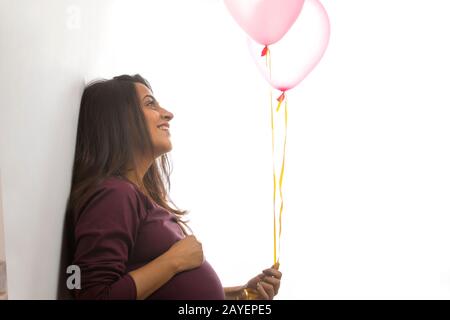 Schwangere Frau lächelt an den rosafarbenen Luftballons in der Hand. Stockfoto