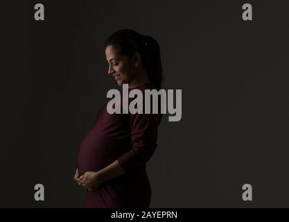 Schwangere Frau lächelt mit ihren Händen an ihrem Babybump. Stockfoto