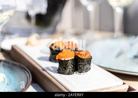 Auf einer kleinen Holztafel in einem Tisch mit Weingläsern und einer Flasche Wein auf einer Terrasse eines Restaurants im Freien werden Sushi-Speisen mit Fischeiern serviert. Stockfoto