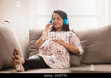 Schwangere Frau ruht auf dem Sofa und hört Musik. Stockfoto