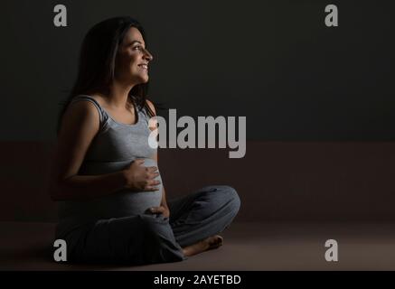 Schwangere Frau denkt über ihr Baby nach und lächelt. Stockfoto