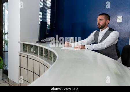 Stock-Foto eines jungen Mannes in Uniform, der an einer Hotelrezeption arbeitet Stockfoto