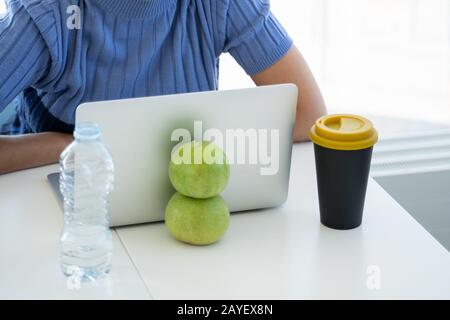 Zwei grüne Äpfel, Wasser und ein Kaffee vor einem Laptop in einer Coworking Stockfoto