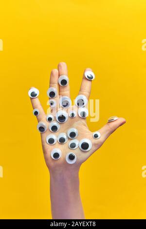 Hand der Frau mit Plastikaugen auf gelbem Hintergrund. Stockfoto