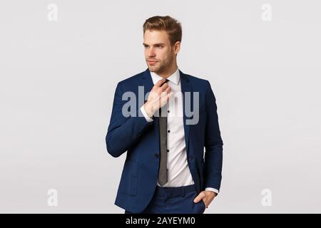 Der elegante Geschäftsmann in blauer Classis Anzug passt die Krawatte an und sieht weg, hält die Hand in der Tasche und macht sich bereit Stockfoto