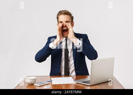 Ausdrucksstarker und emotionaler junger blonder Mann sitzt im Büro und fühlt sich unter Druck gesetzt. Geschäftsmann mit schlechtem Temperament, der laut schreit, ca. Stockfoto
