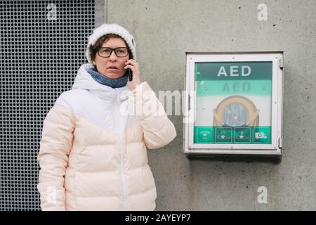 Notruf zur kardiopulmonalen Reanimation. Kaukasische Frau telefoniert mit Notrufhilfe. Gerätebox aed automatisch Stockfoto