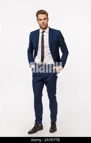 Durchgehender, vertikal aussehender, durchsetzungsfähiger Geschäftsmann im klassischen Anzug, hält die Hände in der Hose und sieht aus, wie die Kamera verwirrt Stockfoto