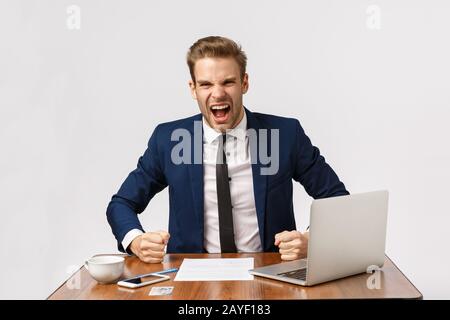 Ausdrucksstarker und empörter junger blonder Geschäftsmann punzelt aggressiv und schreit Geschäftspartner, fühlt sich enttäuscht Stockfoto