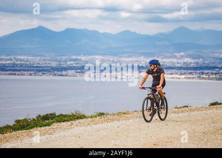 Junger Kerl, der in Spanien auf einem Fahrradweg mit dem Mountainbike-Rad unterwegs ist. Athlet auf einem Mountainbike-Rad fährt vor dem Hintergrund o im Gelände Stockfoto