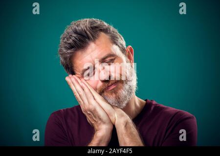 Ein Porträt eines bärtigen Mannes in rotem T-Shirt mit Schlaf-Geste. Konzept "Menschen und Emotionen" Stockfoto