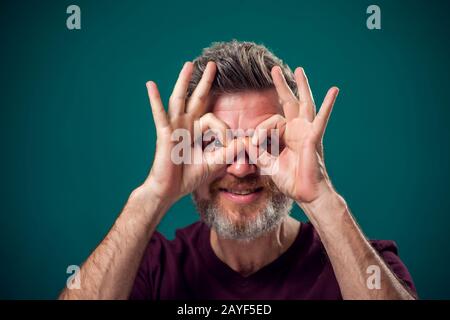 Ein Porträt eines bärtigen glücklichen Mannes, der Eulengeste in rotem T-Shirt zeigt. Konzept "Menschen und Emotionen" Stockfoto