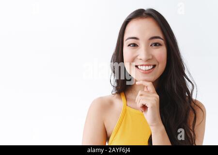 Nahaufnahme von nachdenklichen und fröhlichen jungen, intelligenten ostasiatischen Unternehmerinnen, die neue Konzepte für ihr Geschäft abdenken und dabei das Kinn nachdenklich berühren Stockfoto