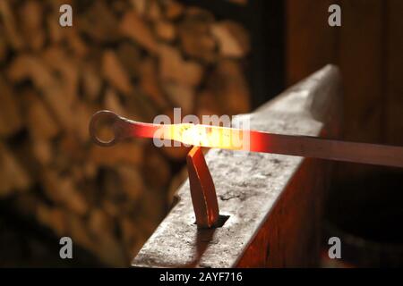 Ein Schmied verwendet einen Hammer, um ein glühendes Metallstück auf dem Amboss zu bearbeiten Stockfoto