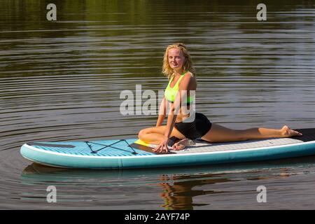 Junge Frau in Yoga-Schwan-Haltung auf SUP Stockfoto