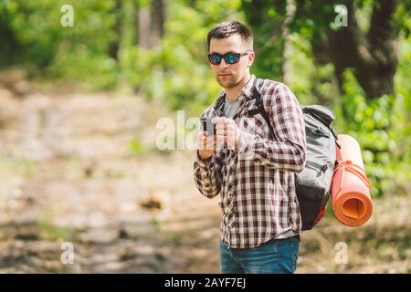 Hipster junger Mann mit Rucksack mit Smartphone auf wunderschönem Naturerlebnis.Reisekonzept. Reisen im Freien. Reisen und erkunden. Backpa Stockfoto