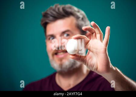 Ein Porträt eines bärtigen Mannes, der weißes Ei in der Hand hält. Menschen- und Lebensmittelkonzept Stockfoto