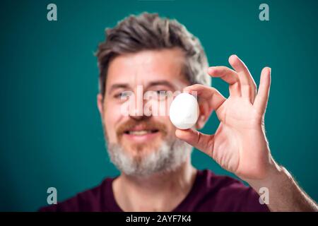 Ein Porträt eines bärtigen Mannes, der weißes Ei in der Hand hält. Menschen- und Lebensmittelkonzept Stockfoto